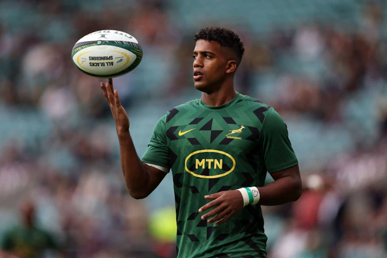 A young man in sports clothing balances a rugby ball on one finger.