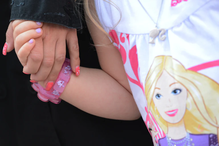 Gros plan d'une femme tenant la main de sa fille, qui porte une montre rose et une chemise à l'effigie de Barbie.