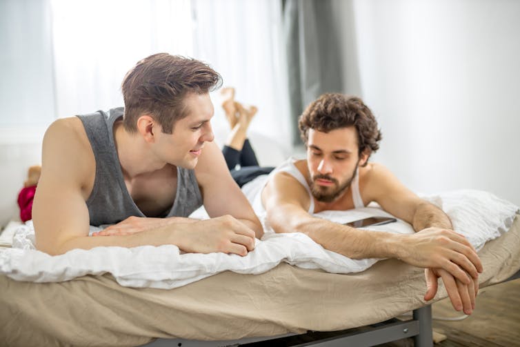 Two men taking in bed together