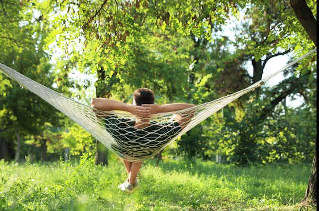 A man resting in a hammock in an overgrown garden.