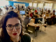 A woman seen in front of a blurred background of students at desks.