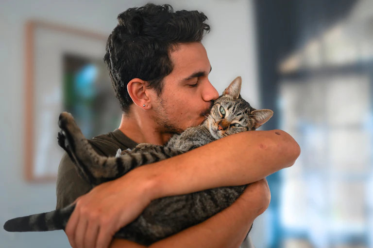 Un jeune homme aux cheveux noirs tenant et embrassant un chat tabby