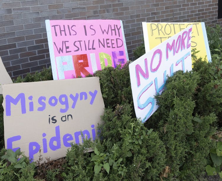 Signs on placards propped on grass that say 'misogyny is an epidemic' and 'no more shit.'
