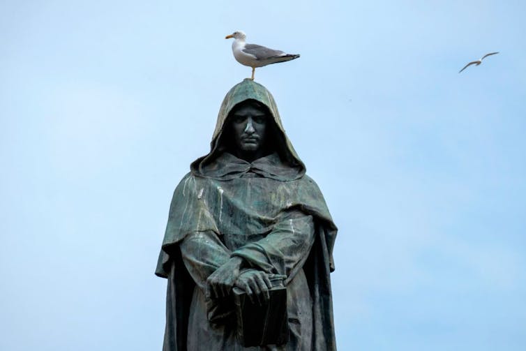A gull rests on the head of a statue of a hooded man.