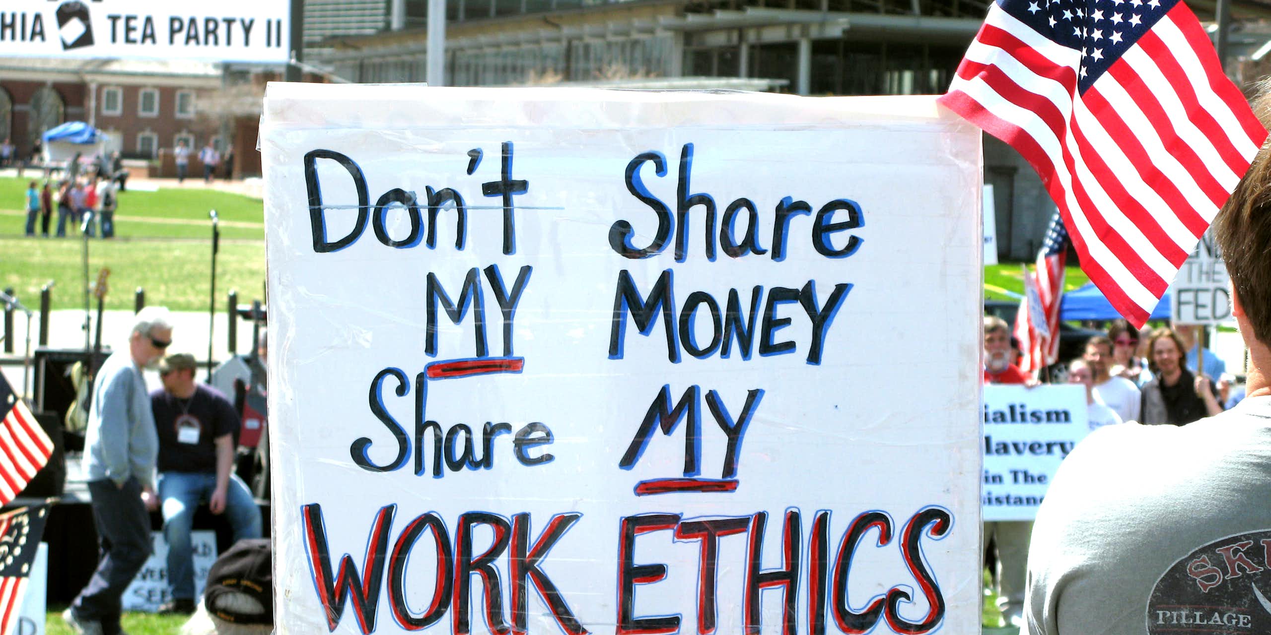 Lors d'une manifestation avec des drapeaux américains, on voit une pancarte proclamant « Don't share my money, share my work ethics ».