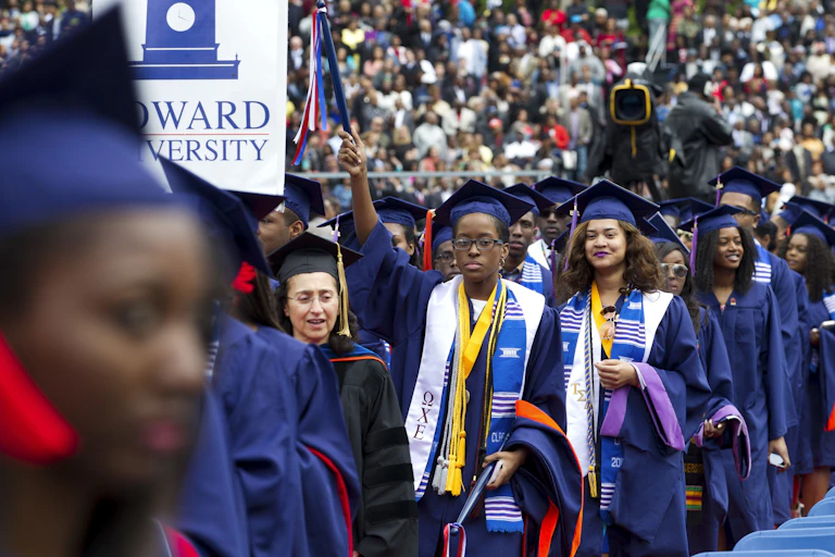 Studens wearing blue caps and gowns assemble at a graduation ceremony.
