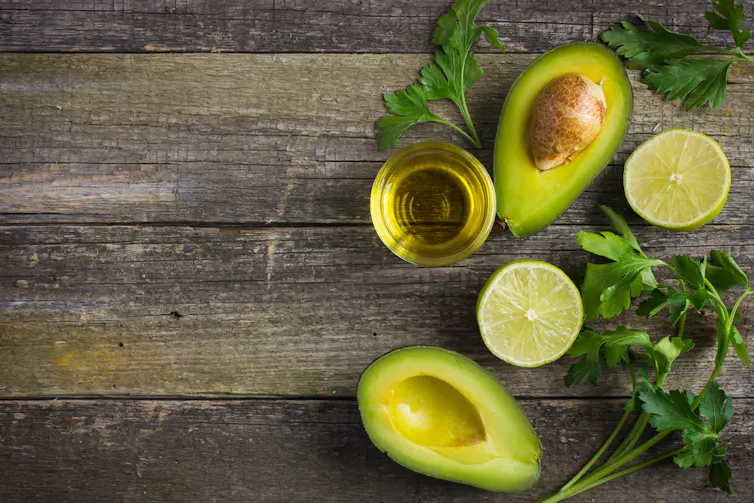 Cut avocado, glass of olive oil, green herbs and cut lemon on timber background