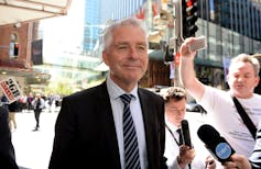 Silver haired man wearing suit leaving court