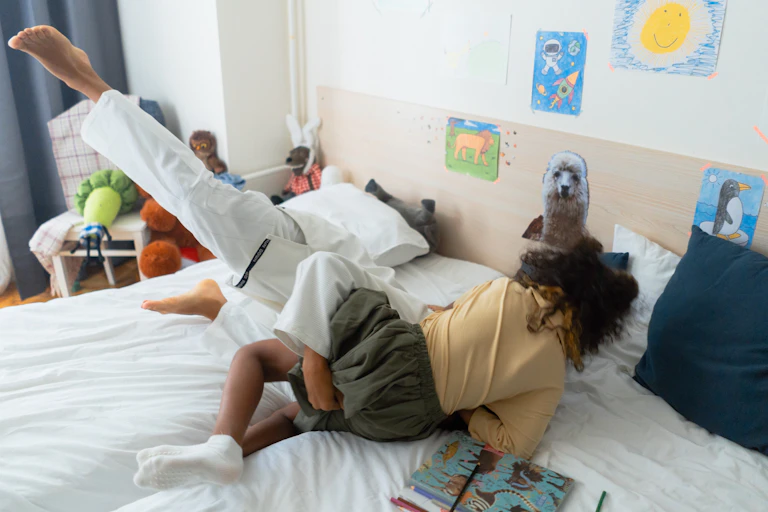 Two children wrestle on a bed.