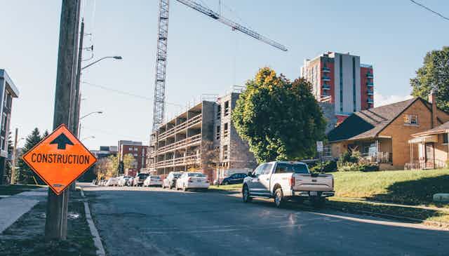 Street with new high-rise development underway next to single-detached houses with a construction road sign in the foreground