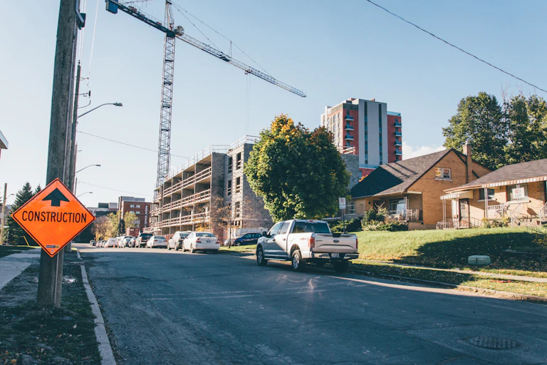 Street with new high-rise development underway next to single-detached houses with a construction road sign in the foreground