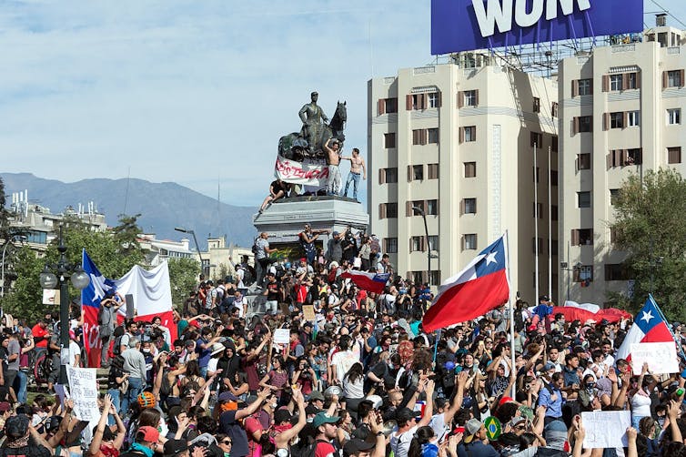 Muchedumbre con banderas de Chile se encarama a una estatua.
