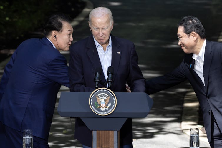 South Korean President Yoon Suk Yeol shakes hands with Japanese Prime Minister Fumio Kishida in front of US President Joe Biden