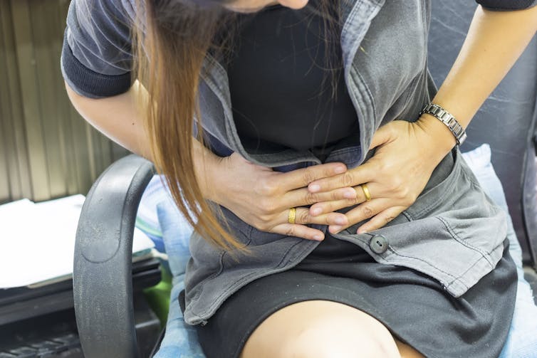 A woman sitting in an office chair holds her stomach in pain.