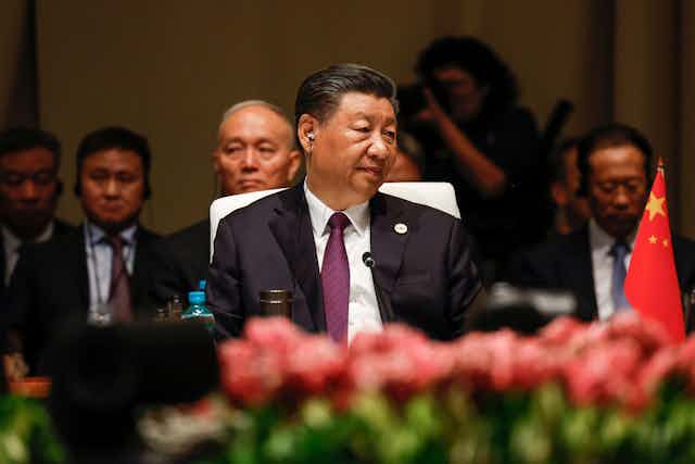 China's president Xi Jinping sits at a table with a microphone.