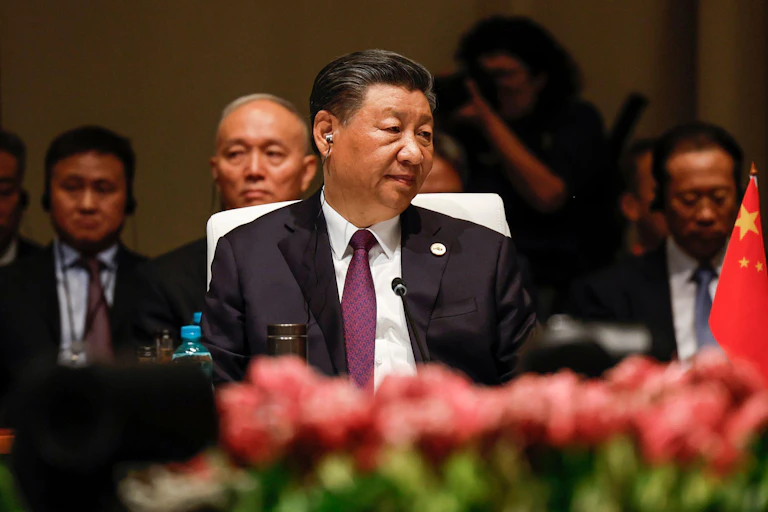 China's president Xi Jinping sits at a table with a microphone.