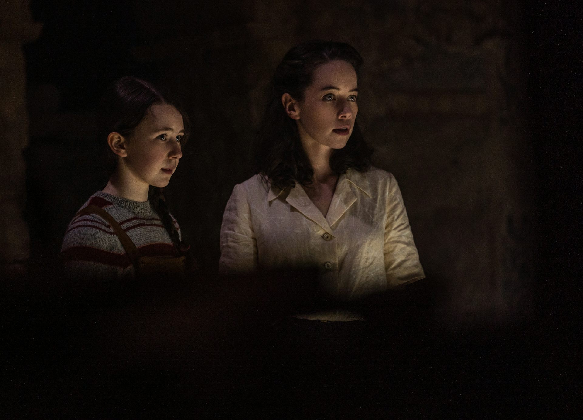 Two young women holding a candle in a dark room.