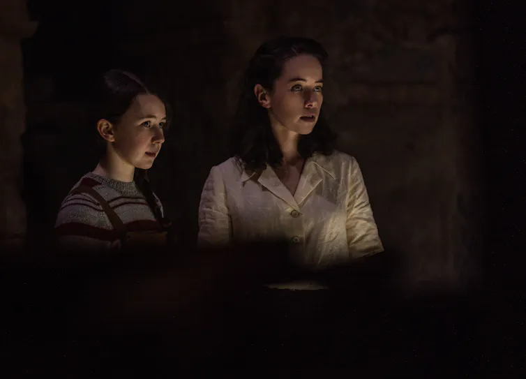 Two young women holding a candle in a dark room.