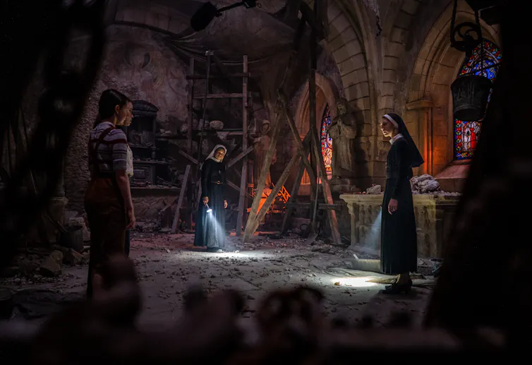 Group of nuns and young women holding torches in a dark room.