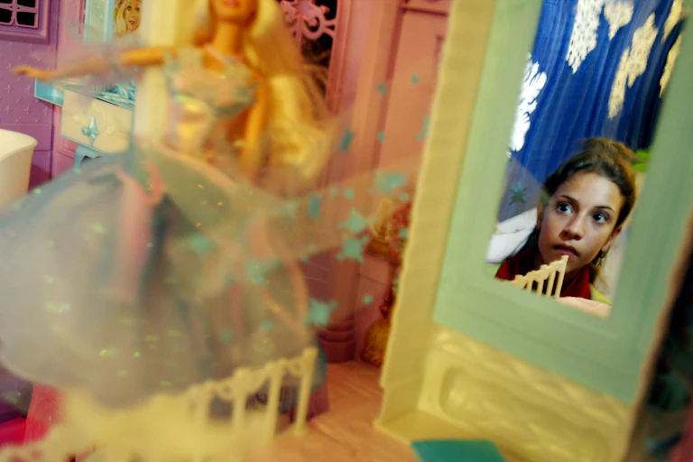 Close-up of Barbie doll on display while mirror reflects image of girl observing it.