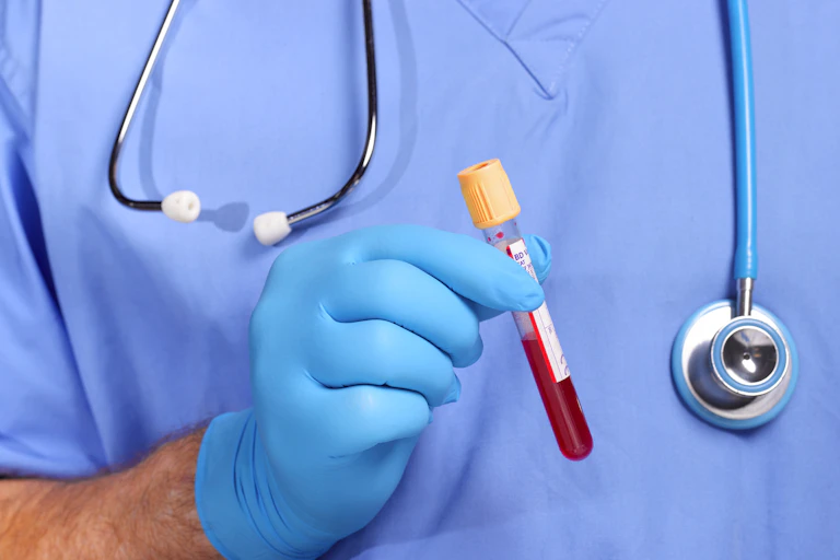 A person wearing scrubs and gloves holds up a test tube filled halfway up with blood.