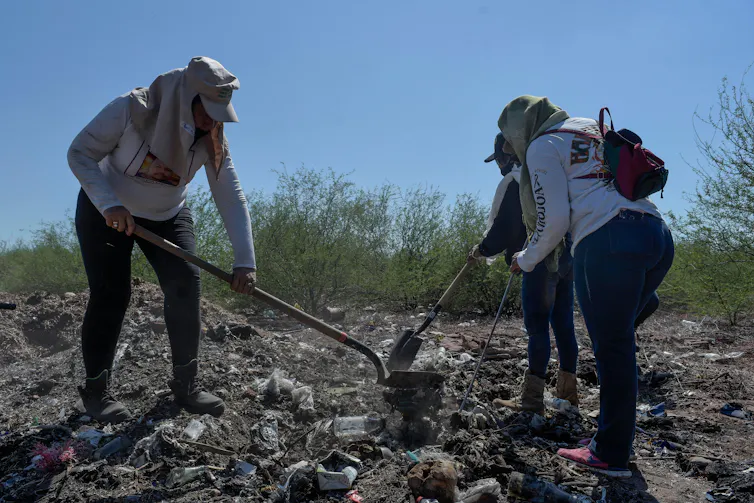 Women digging through possible human remains under the desert sun