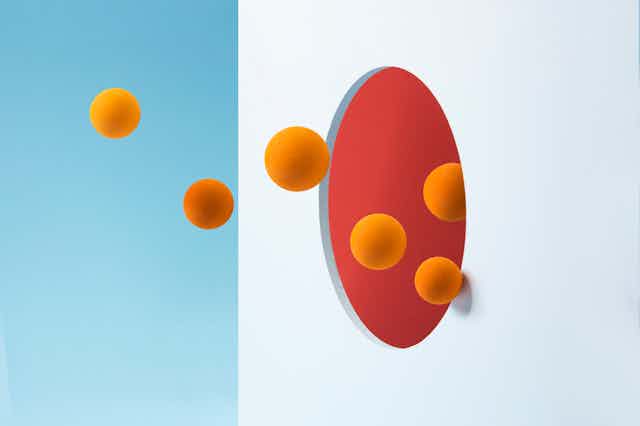 Illustration of orange spheres entering a hole in a white wall with a red interior