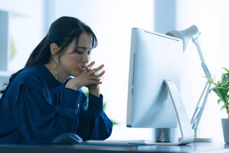 A sad-looking woman sits in front of a desktop computer screen