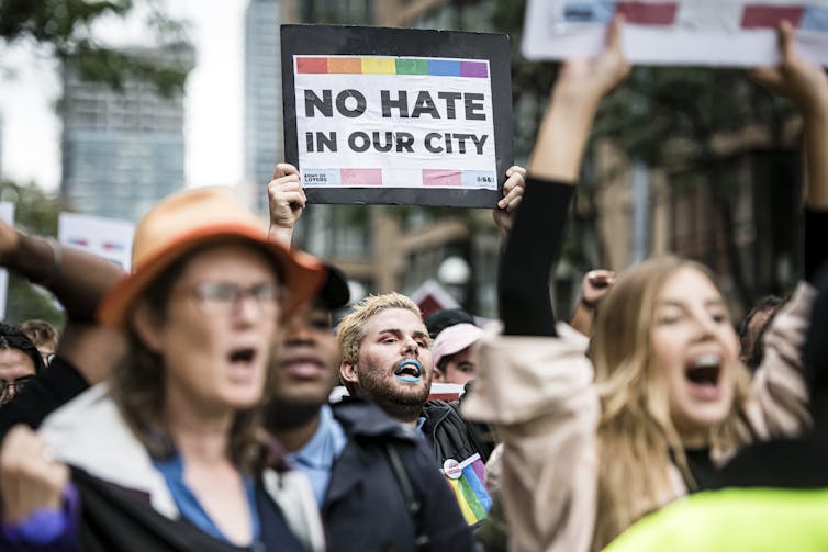 people at a demonstration. A man holds a placard reading: No hate in our city.