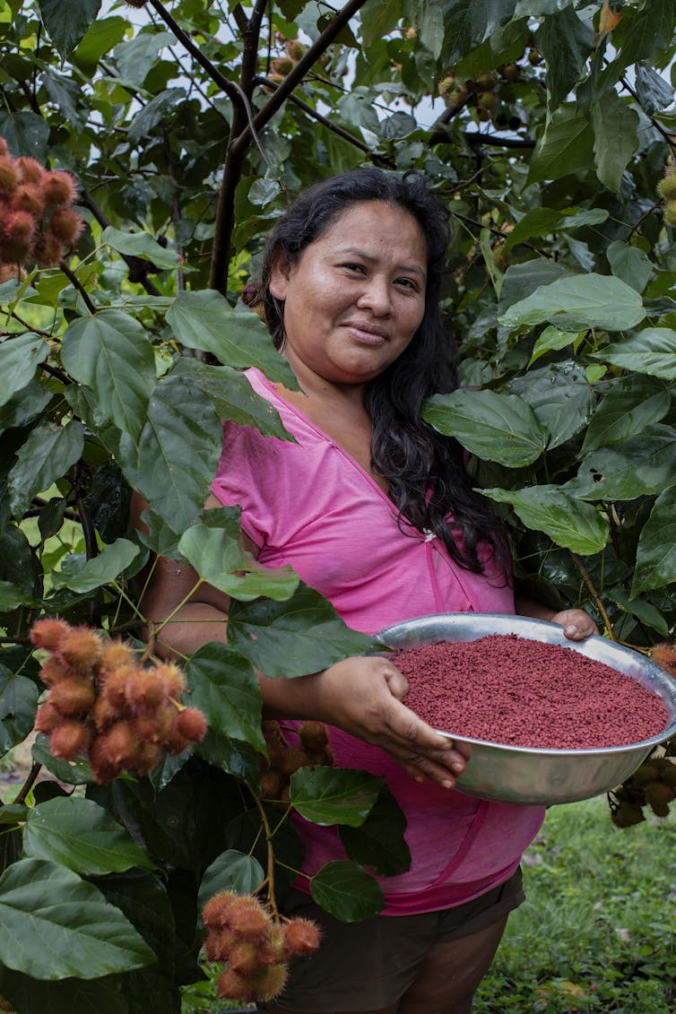 A woman holding a bowl of urucum in a forest.