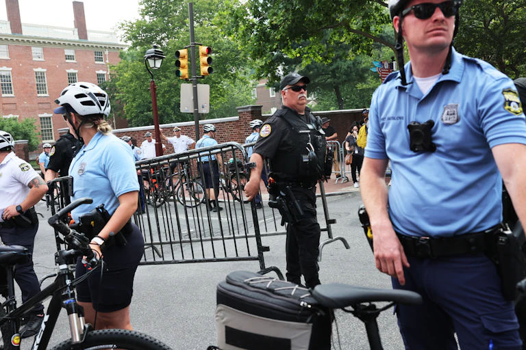 Two police officers stand on a busy street. Each one is wearing a small black box on their chest.