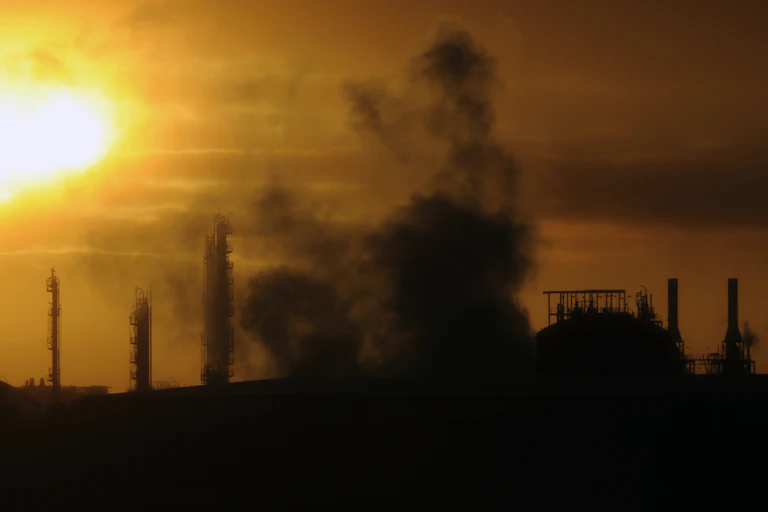 sun rises over smoke emerging from an industrial plant