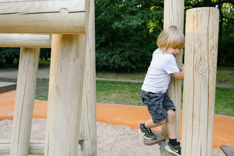 A young child climbs on park equipment.