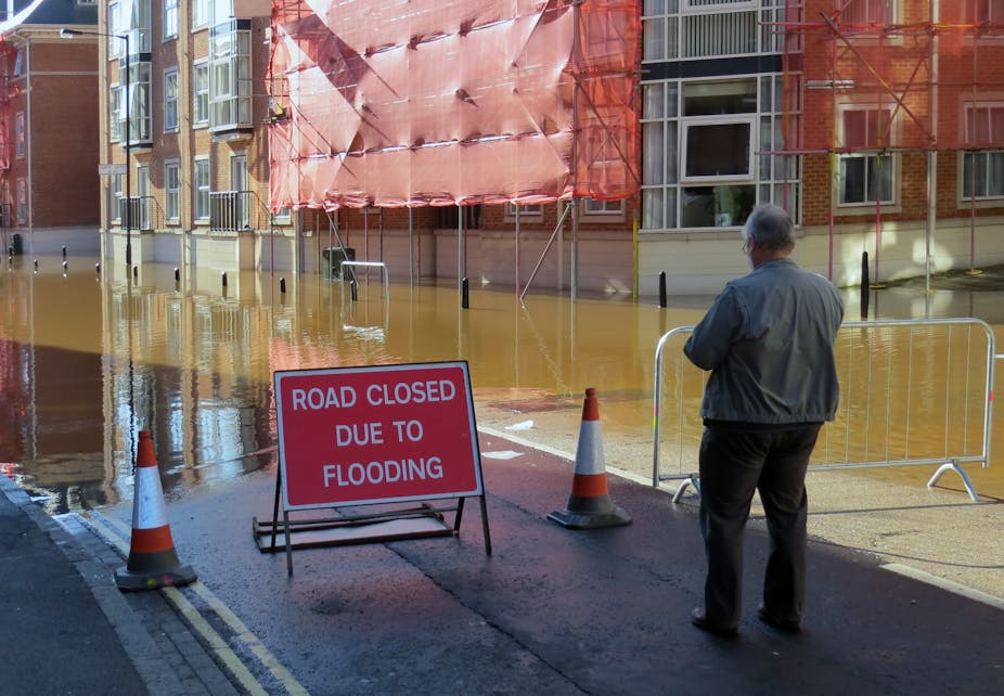 A man stands in a flooded street in front of a sign that says 'road closed due to flooding'. 