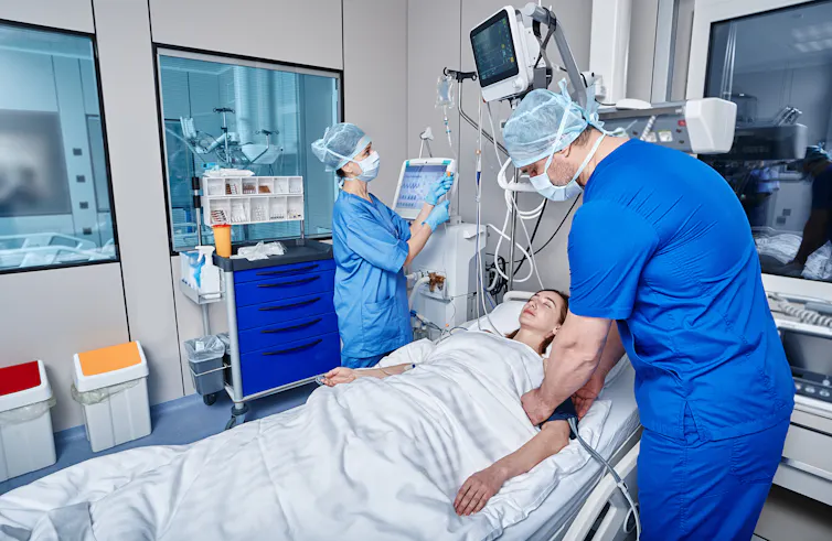 Two intensive care nurses attend to a sick female patient.