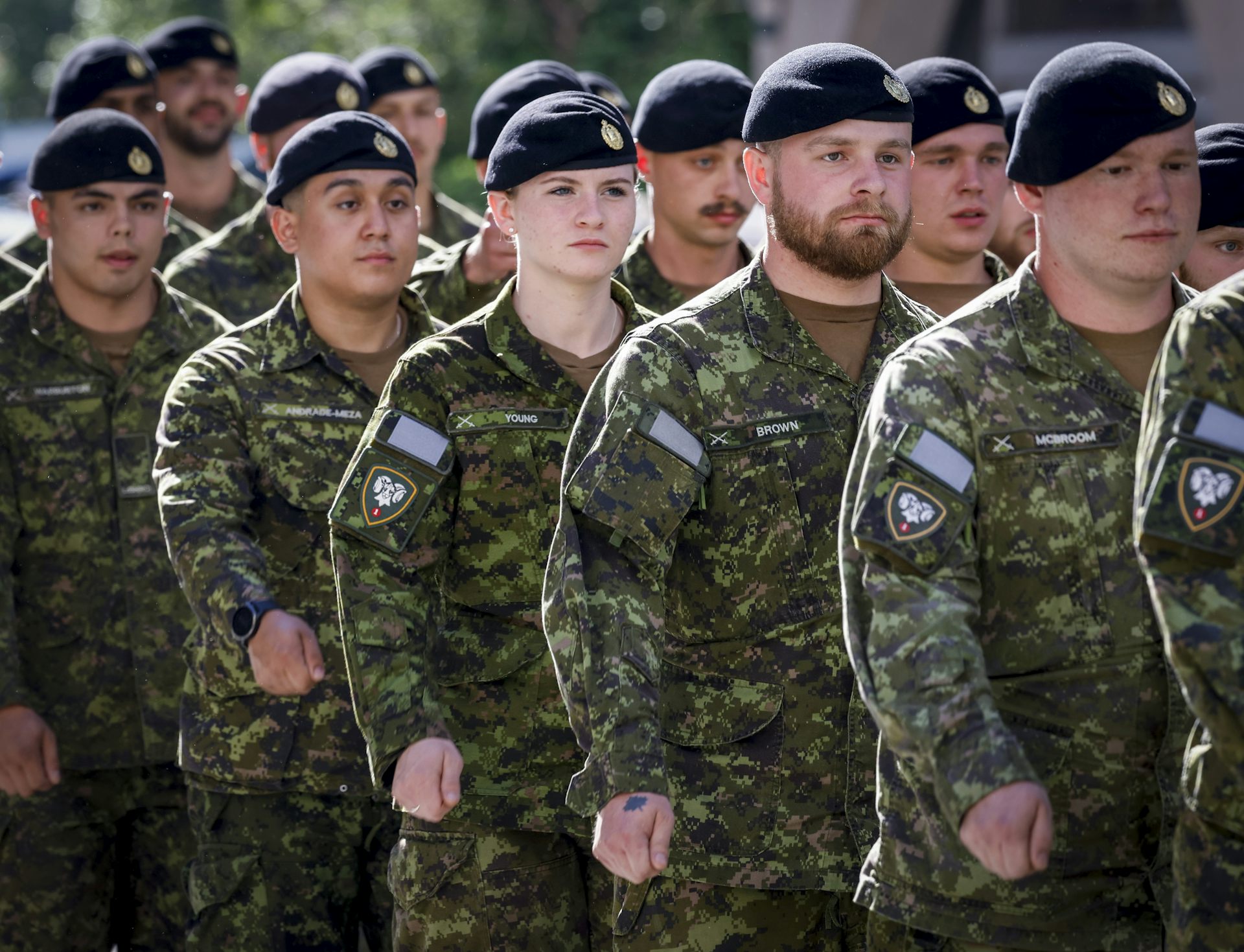 A group of soldiers in military garb walk in a parade, one female soldier among them.