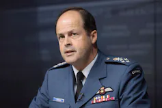 A bald man in a military uniform speaks at a news conference.