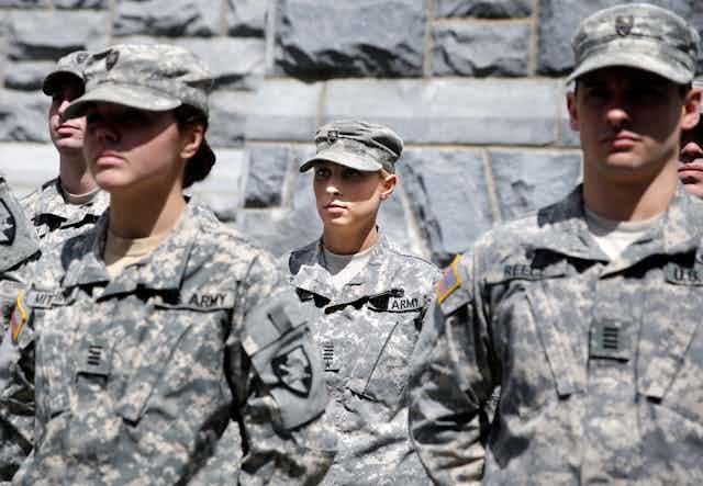 Two male and two female cadets in U.S. army camouflage stand at attention.