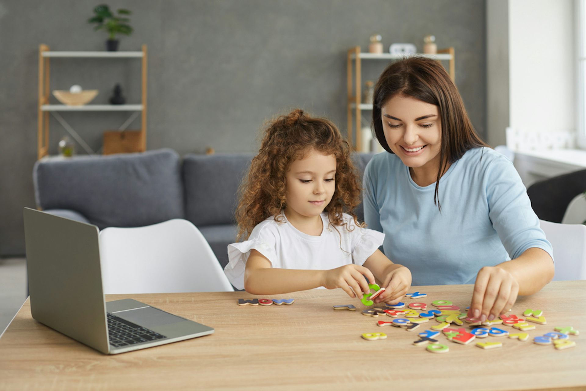 Une petite fille et sa mère assises à un bureau et manipulant des lettres de différentes couleurs