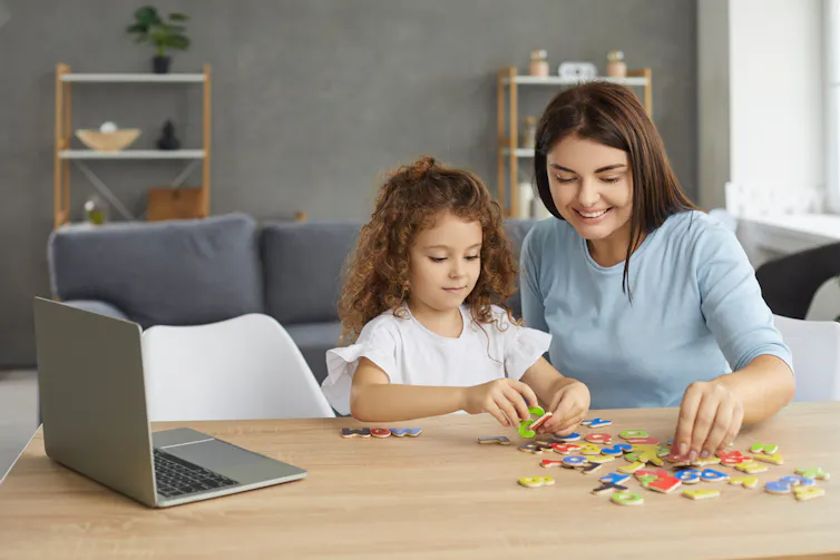 Une petite fille et sa mère assises à un bureau et manipulant des lettres de différentes couleurs