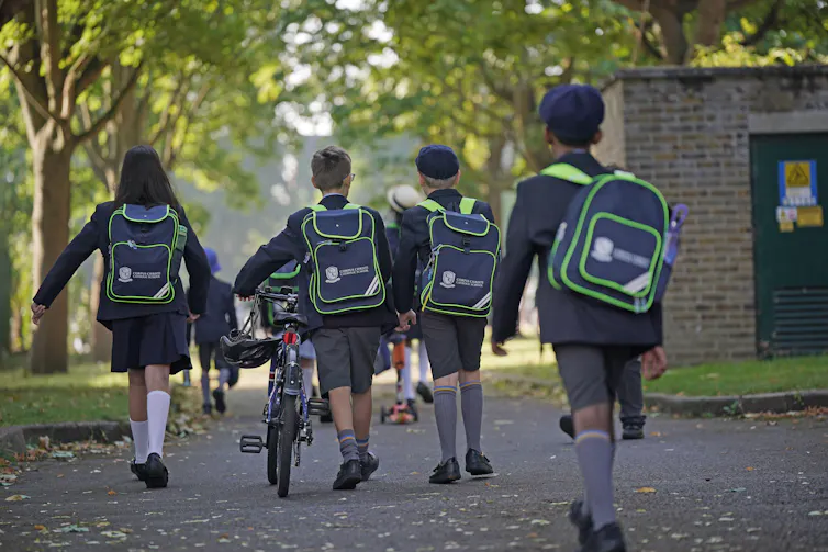Primary school students in full uniform walk along a path.