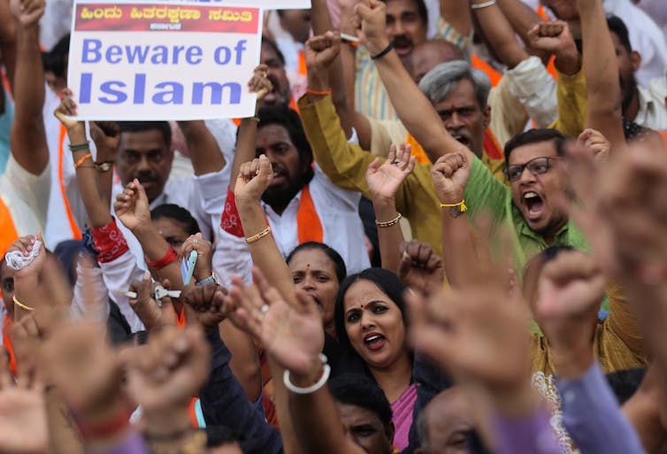 Crowd of people waving their arms and shouting, one carrying a sign reading 'Beware of Islam'.