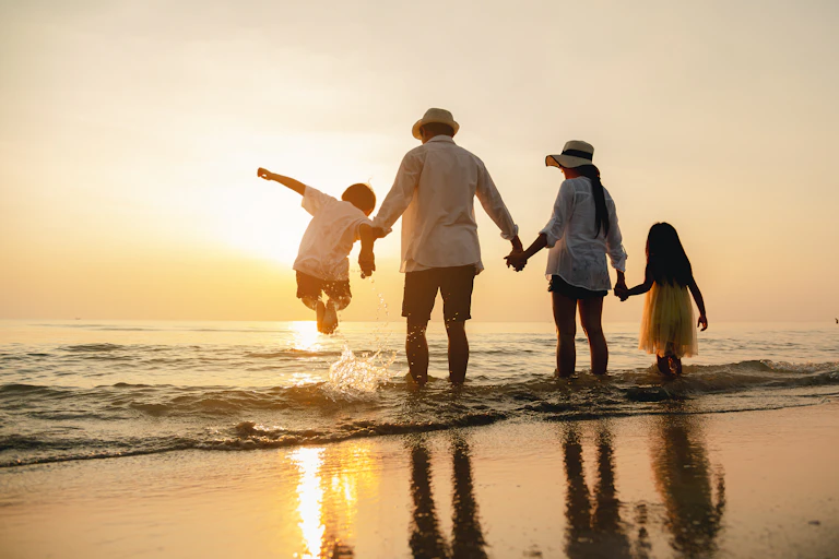 A family of four at the beach holding hands and looking out to sea.