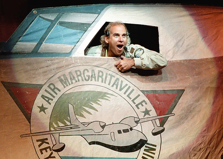Man dressed as pilot shouts out the window of a fake plane with the words 'Air Margaritaville' printed under the cockpit window.