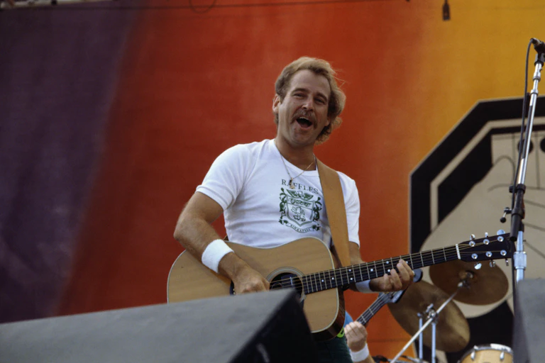 Smiling man plays acoustic guitar on stage.