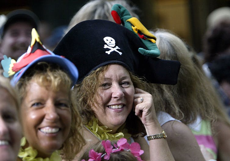 Two smiling women wearing leis and colorful novelty hats.
