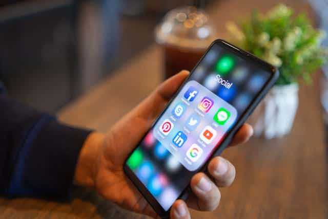 A hand holding a cell phone with social media apps displayed on the screen