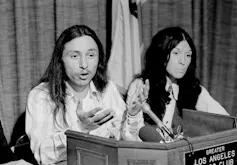 A man and woman seated beside each other behind a podium