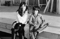 Black and white photo of a woman sitting on a curb with a little boy.