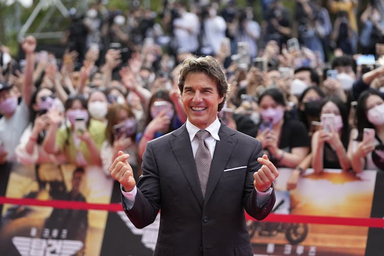 A man in a dressy jacket and tie seen waving in front of fans.